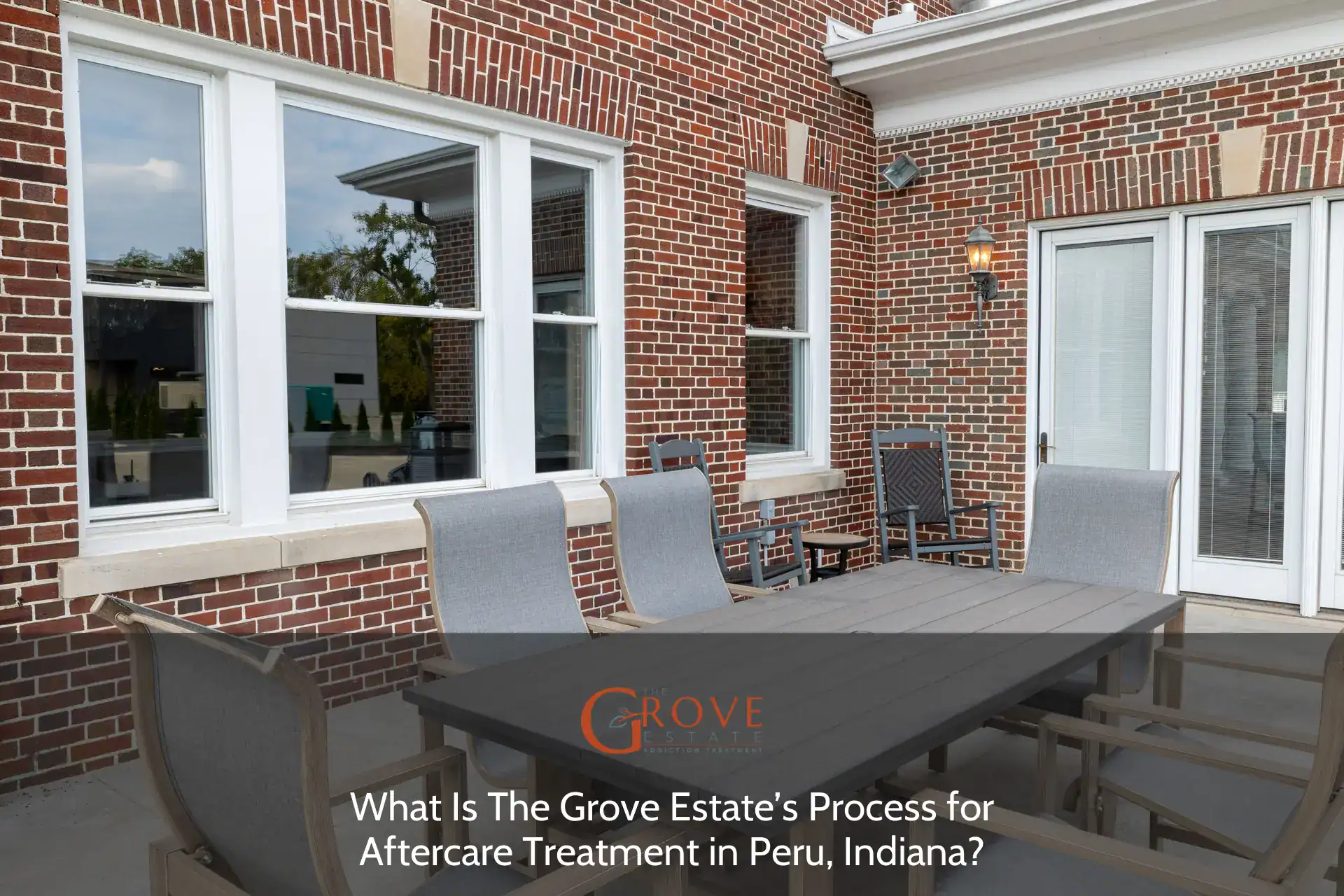 Outdoor dining area featuring a large table and gray seating set against a brick wall, showcasing The Grove Estate’s inviting space in Peru, Indiana.